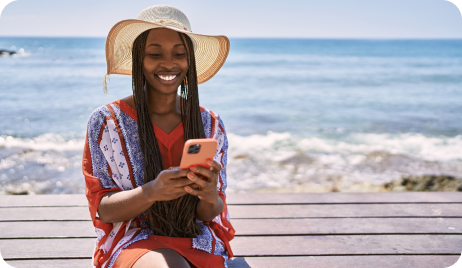 Woman smiling with her cell phone with the sea in the background.