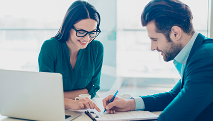 Man signing papers while woman indicates where to sign 