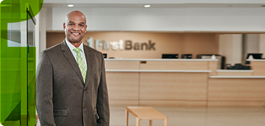 bald man in suit in front of firstbank branch