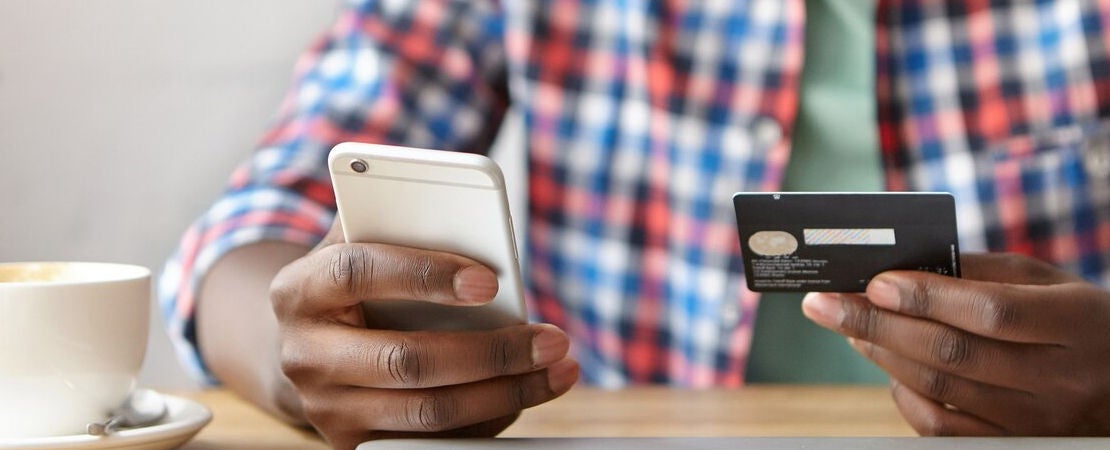 hombre sosteniendo en sus manos un celular y una tarjeta de banco