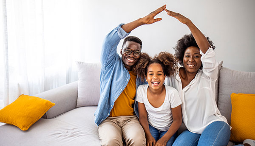 family of three smiling and holding their hands as a house