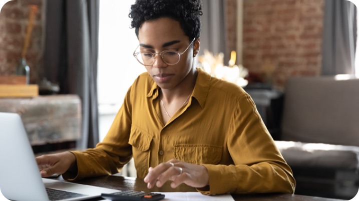 Woman wearing glasses using a calculator in front of laptop.