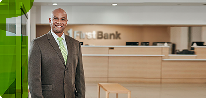 hombre calvo de traje frente a sucursal de firstbank