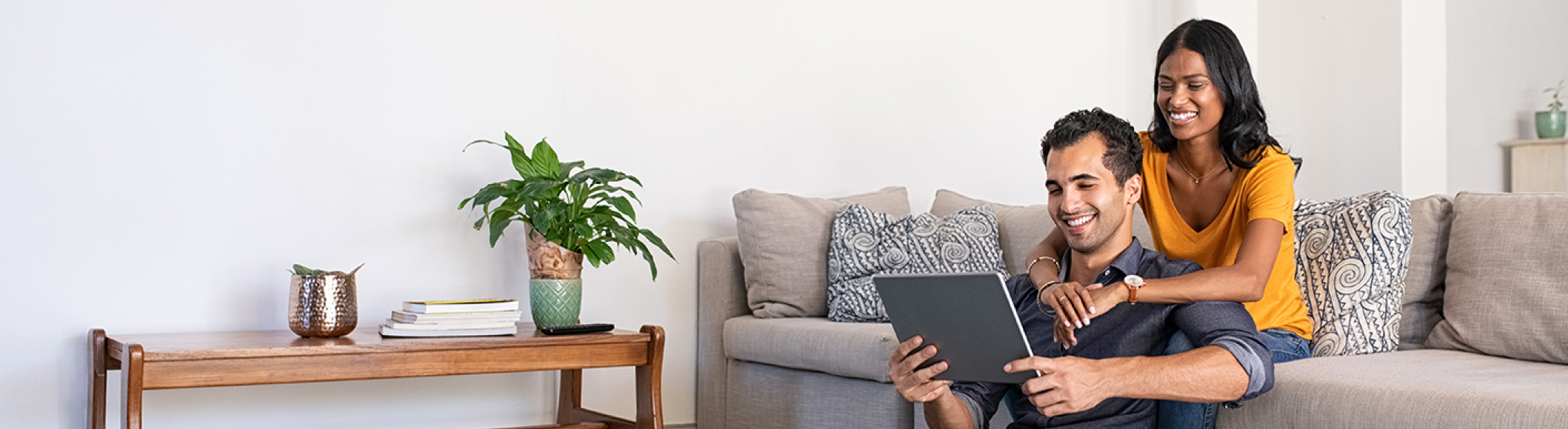 smiling couple sitting in a living room looking at a tablet