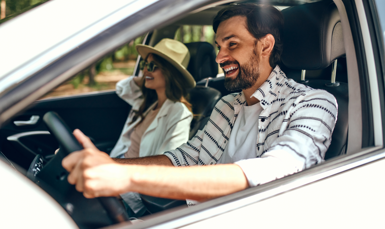 Man driving his car while smiling with his partner as co-driver.