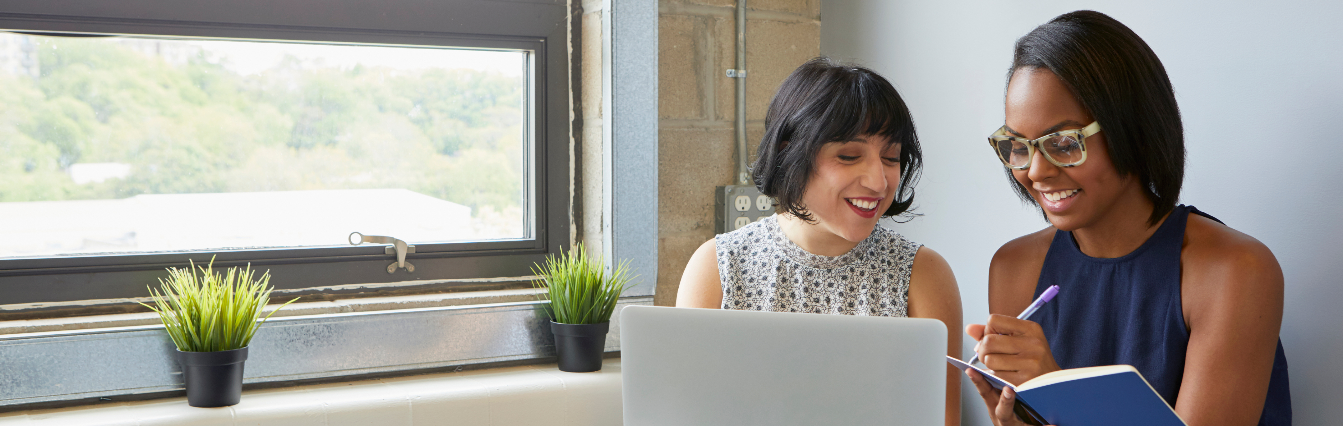 Two women laughing and writing in notebook