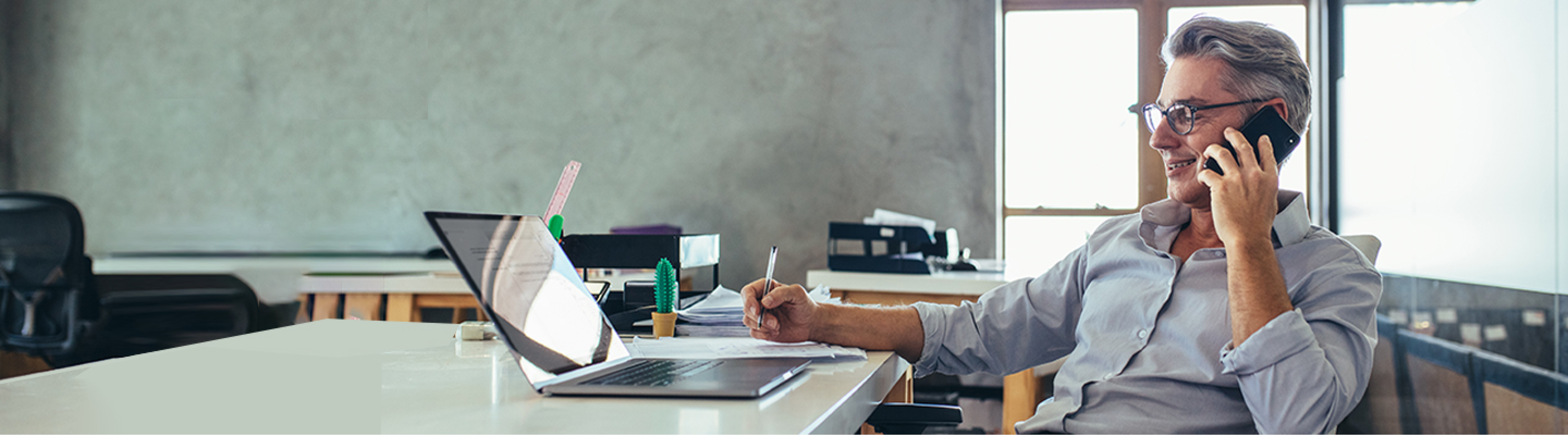 Man talking on the cell phone while writing down something on a piece of paper.